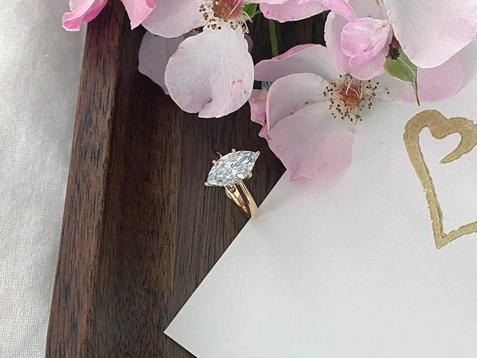 Goldener Verlobungsring mit Navette-Diamant neben Blüten